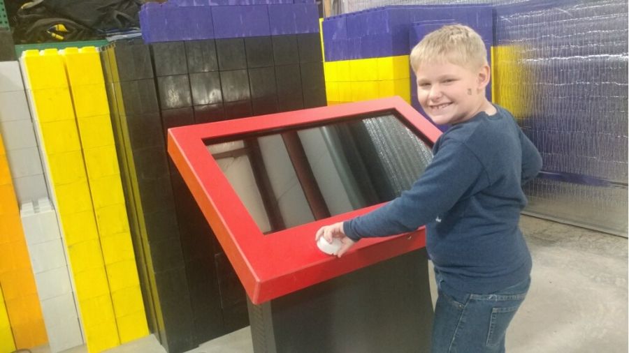 Boy smiling at camera standing in front of a Giant Etch A Sketch